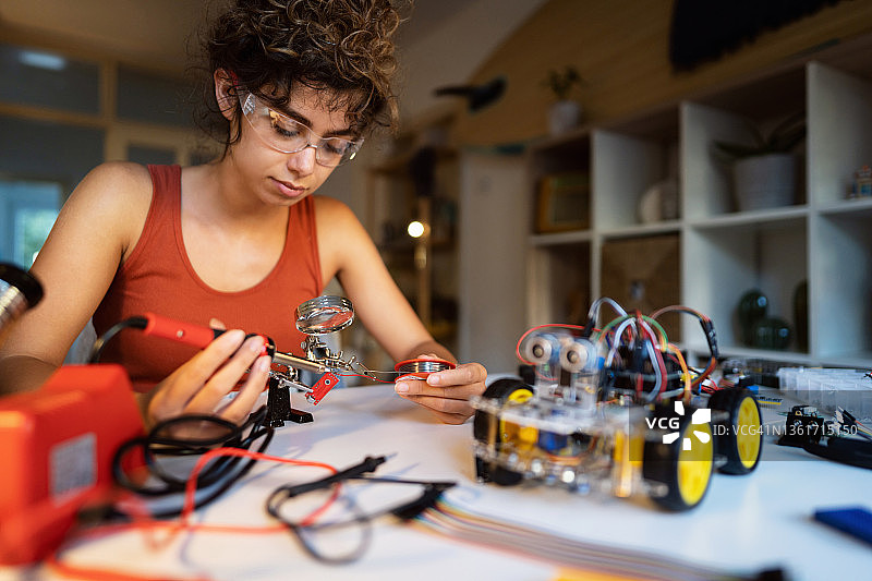 使用放大镜将电线连接到机器人汽车部件上的女性机器人工程师图片素材