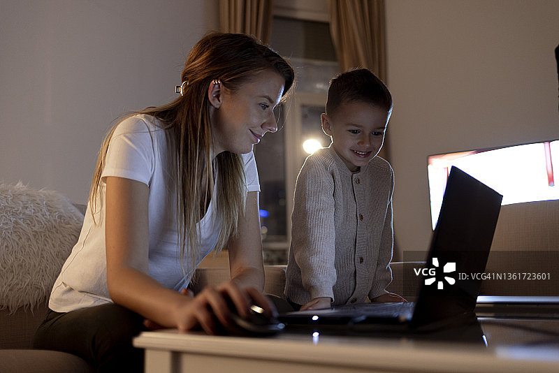在家工作，抱着年幼的儿子使用笔记本电脑的女人图片素材