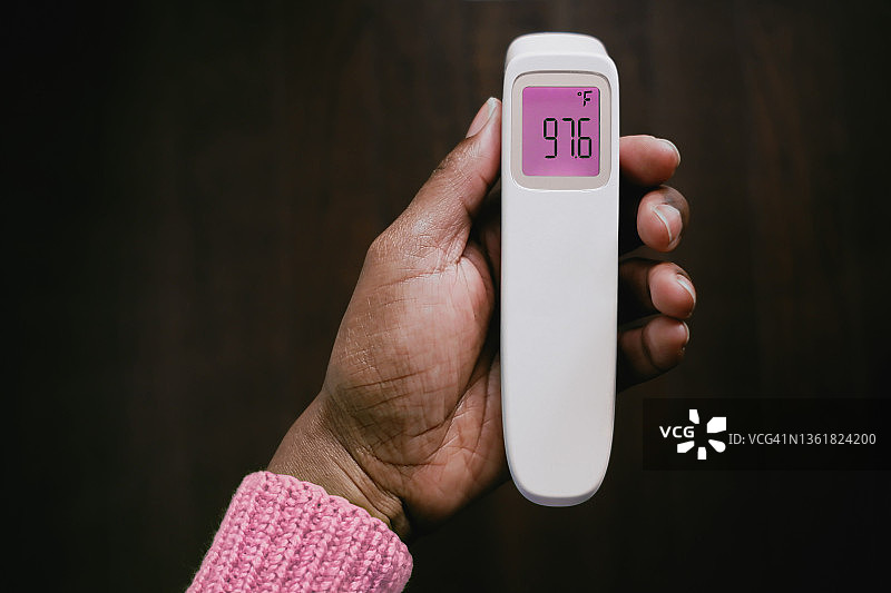 没有发烧:女子手持红外体温计显示正常体温图片素材
