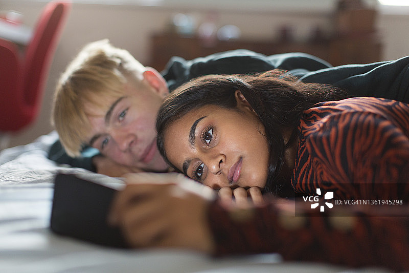 躺在床上使用智能手机的青少年情侣图片素材