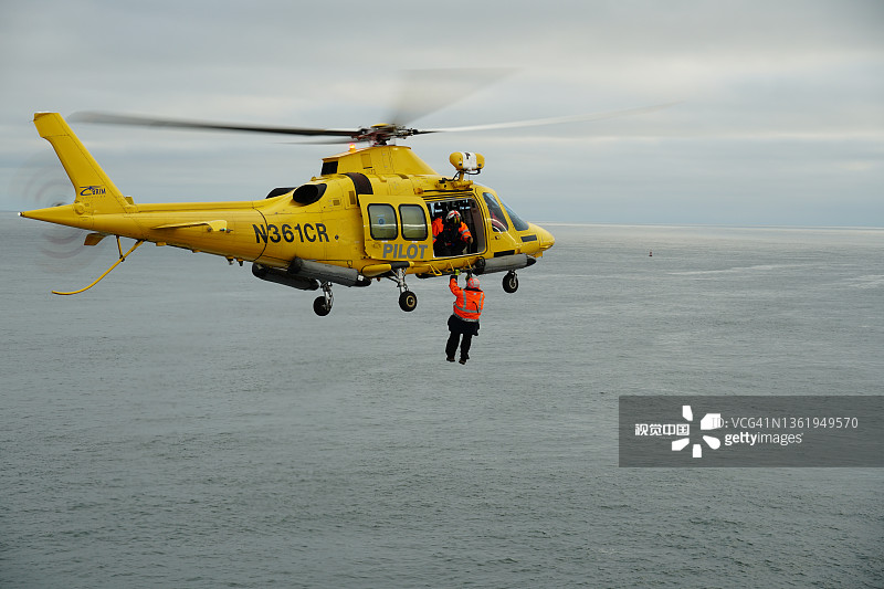 悬挂飞行员准备登上商船集装箱船的黄色直升机图片素材