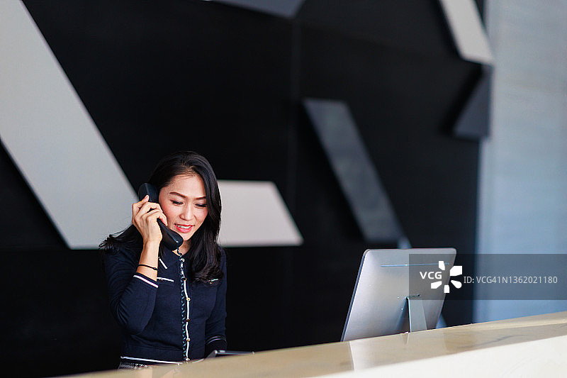 亚洲女性在前台接听酒店电话图片素材