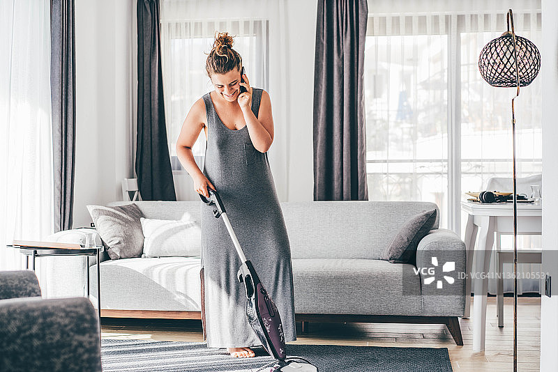 女人做家务：一边用手机聊天，一边用吸尘器打扫地板图片素材