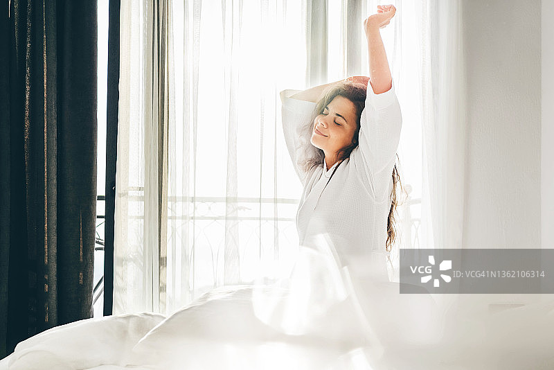 醒来后坐在软床上伸展双臂的长卷发女人图片素材