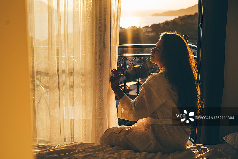 年轻卷发女人穿浴袍拉开窗帘图片素材