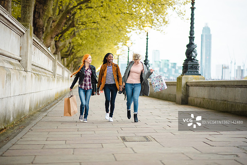在伦敦人行道上行走，手提购物袋的快乐年轻女性图片素材