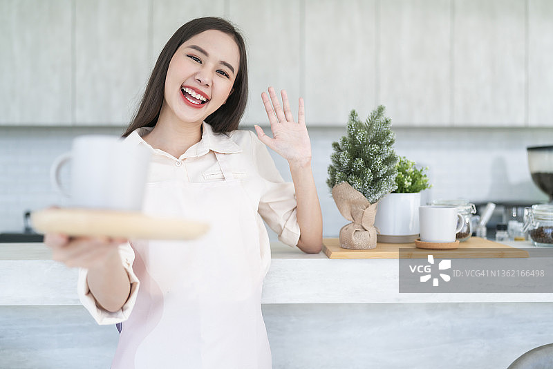 幸福快乐的亚洲女咖啡店主，身穿制服在咖啡店工作，中国女咖啡师向镜头打招呼，表示欢迎，面带微笑，喜悦图片素材