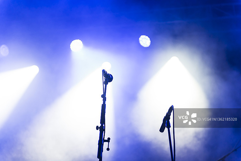 舞台上的两个麦克风支架，在蓝色戏剧烟雾和聚光灯下图片素材