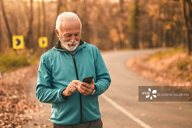 在风景优美的道路上使用手机的快乐老年运动员图片素材