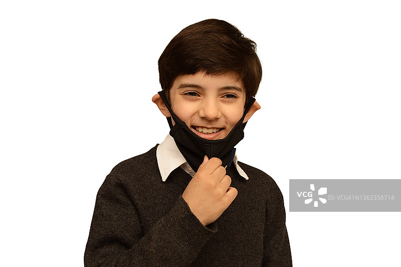一张无忧无虑的微笑的9岁印度亚洲男孩儿童的照片抠图，用手拉着黑色织物面部保护口罩，在白色背景上露出孩子露齿的笑容图片素材