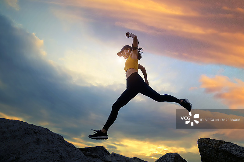 日落时分，亚洲女性在山脊上奔跑跳跃图片素材