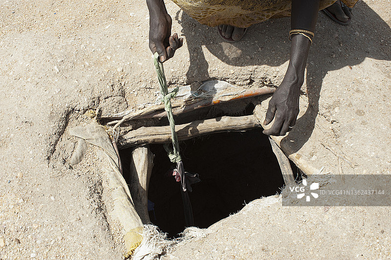 在南苏丹上尼罗州旱季期间，一名妇女伸手到坑里取水图片素材
