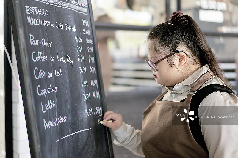 咖啡店里患有唐氏综合征的男人在黑板上写菜单图片素材