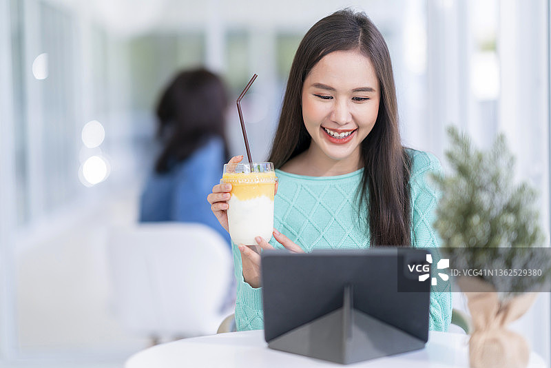 在咖啡馆工作的年轻漂亮的亚洲自由职业女性，手拿冷饮视频通话图片素材