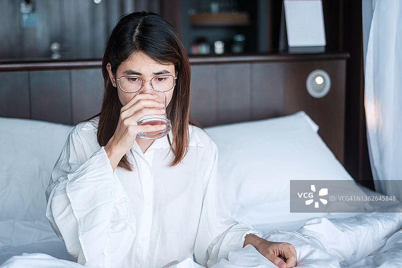 快乐的女人拿着水杯在床上喝水图片素材