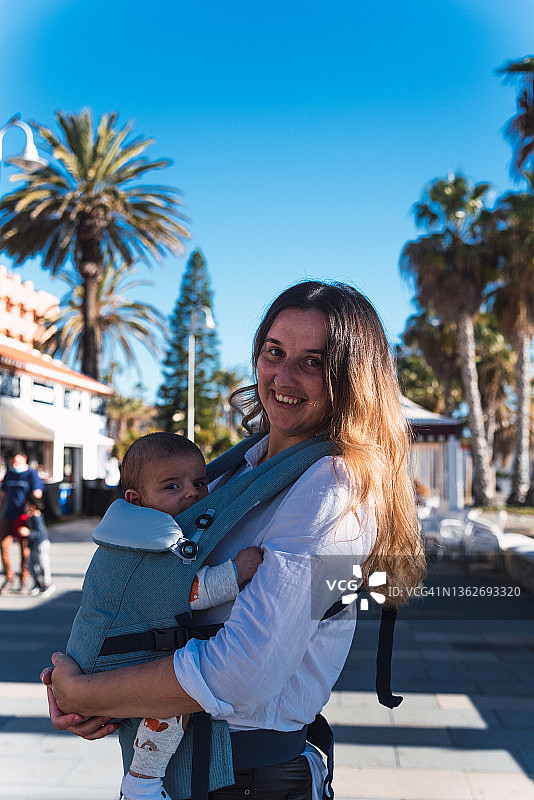 年轻女人在长廊上用婴儿背带带着宝宝散步图片素材