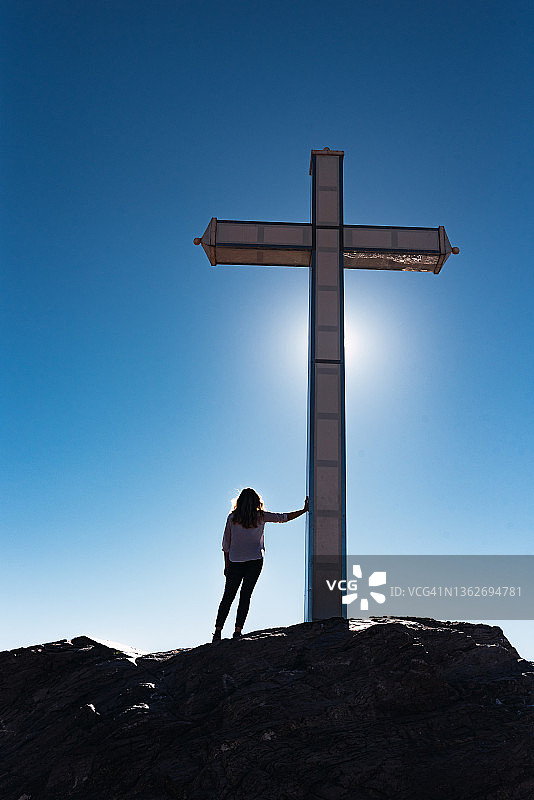 女人倚靠在一个大型基督教十字架上，眺望地平线图片素材