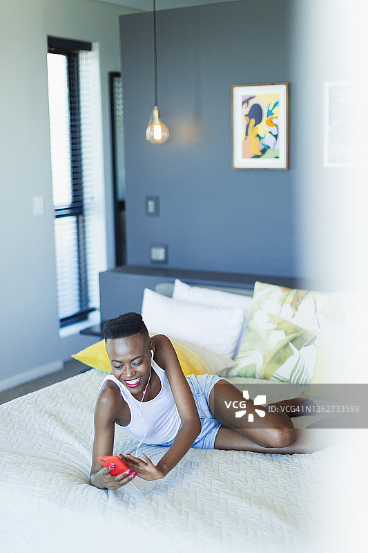 在床上放松，戴着耳机和 mp3 播放器听音乐的微笑年轻女子图片素材