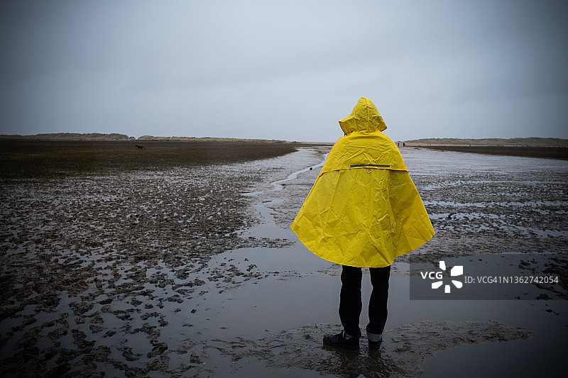 青少年男孩在海滩上穿着黄色外套的背面图图片素材