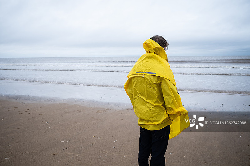 青少年男孩在海滩上穿着黄色外套的背面图图片素材