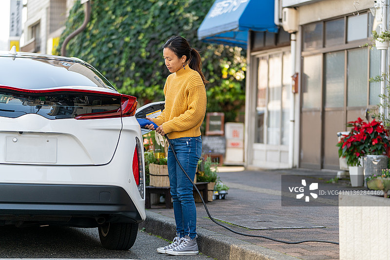 中年妇女插上电动汽车充电图片素材