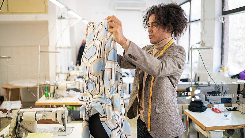 非洲裔美国男裁缝在他的工作室工作，测量手工制作的时尚服装，多元化和融合的概念，新的小型社会企业图片素材