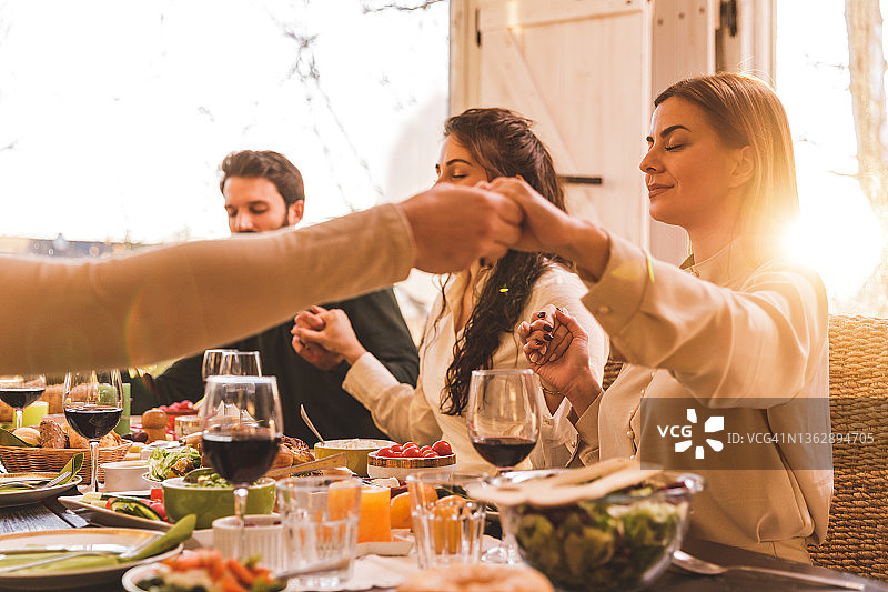 朋友们手牵着手，在享用圣诞晚餐前祷告图片素材