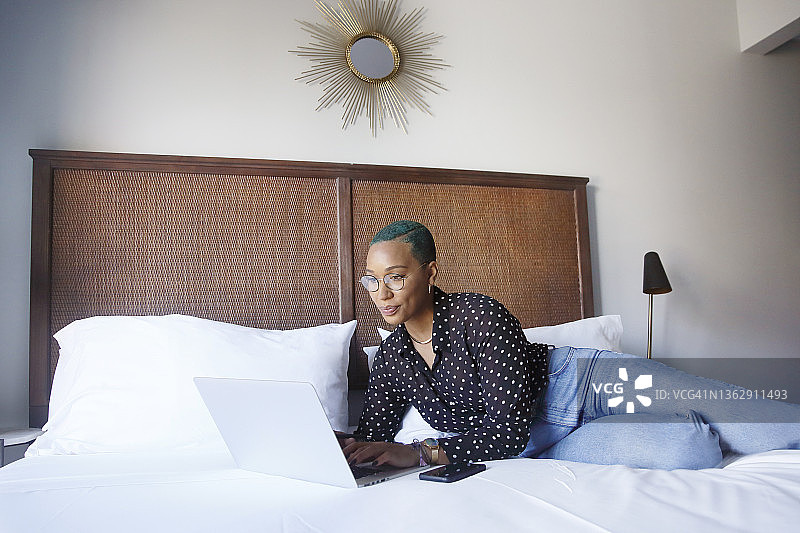 染着绿色头发的混血千禧一代女性在卧室里用笔记本电脑工作图片素材