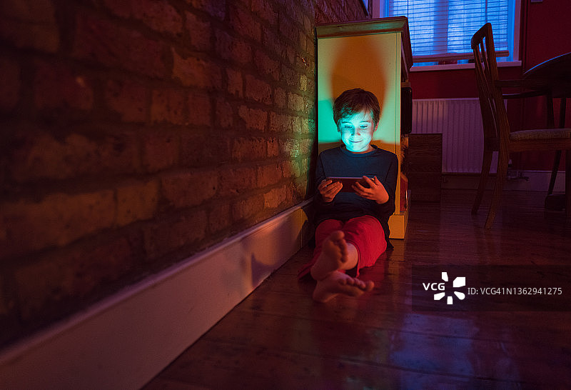 男孩靠在书柜上，晚上看着智能手机图片素材
