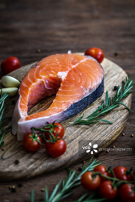 三文鱼：配有番茄、迷迭香和大蒜的生鳟鱼排，置于木桌上图片素材