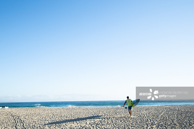 单人桨板手将板和桨运过沙滩，在晨光中投下长长的影子图片素材