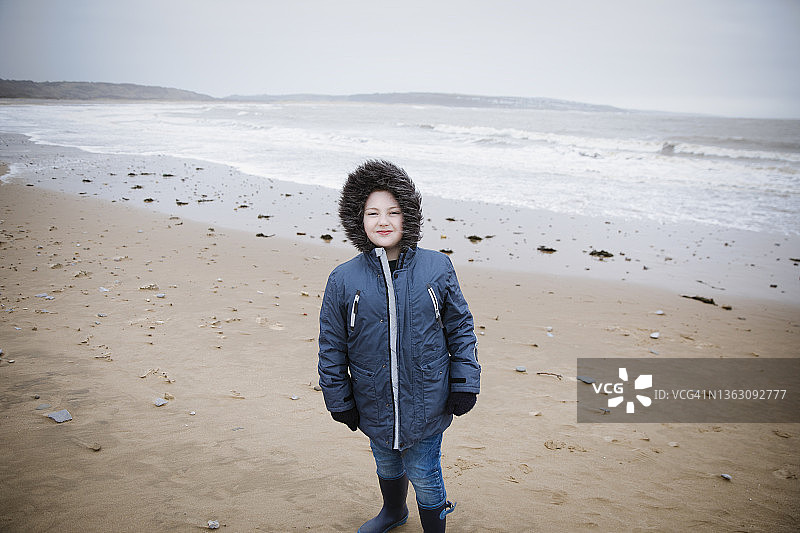 冬季海滩身穿毛皮连帽夹克的自信男孩肖像图片素材