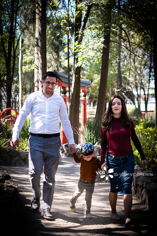 一个年轻的犹太家庭带着一个小孩在公园里走向镜头图片素材