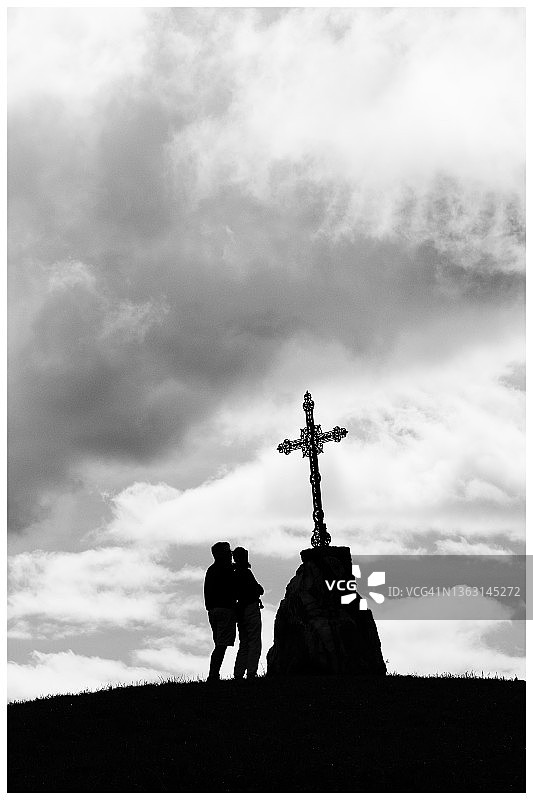 两人组成情侣，在基督教十字架前祈祷。图片素材