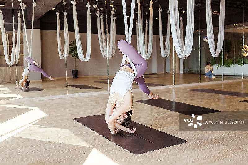 瑜伽房里悬挂的布和练习悬挂瑜伽的年轻女子图片素材