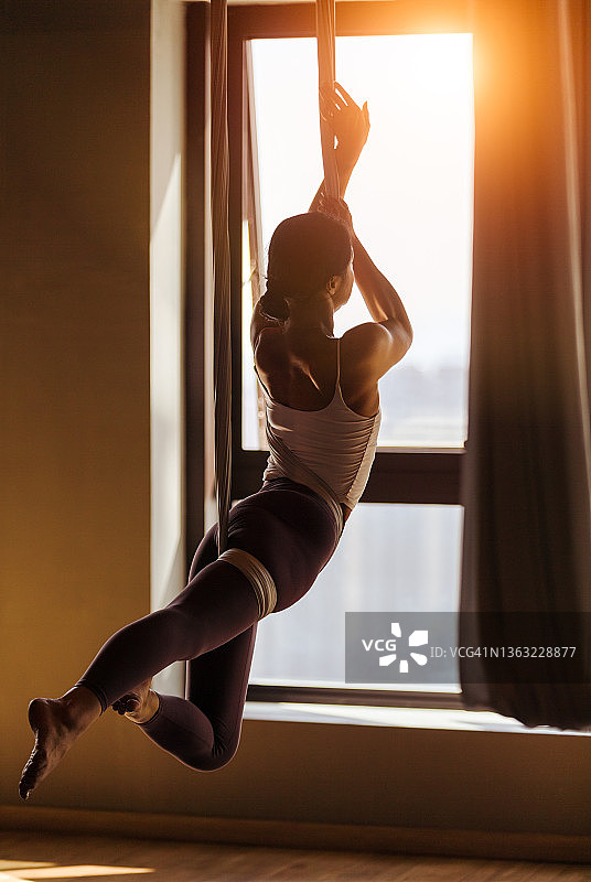 瑜伽房里悬挂的布和练习悬挂瑜伽的年轻女子图片素材