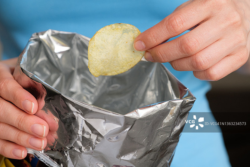 女孩从包装袋中取出香脆的油炸薯片，她正在吃薯片，不健康饮食和生活方式导致体重超标图片素材