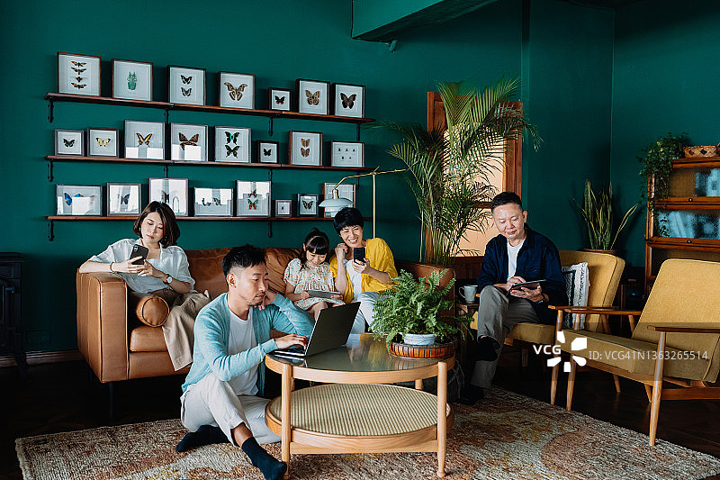 亚裔多代同堂家庭在家中客厅放松身心，使用各种无线技术图片素材