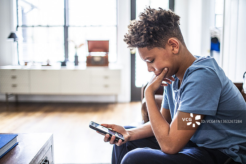 在住宅客厅使用智能手机的青少年男孩图片素材