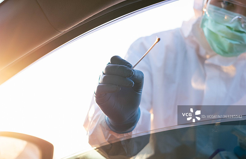 医生身穿防护服在医院入口处为司机进行新冠病毒检测图片素材
