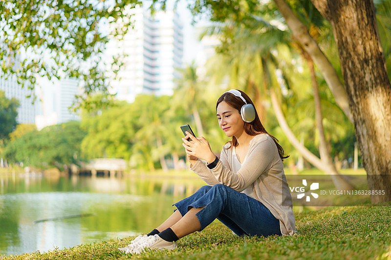 亚裔女子在城市公园听音乐放松心情图片素材