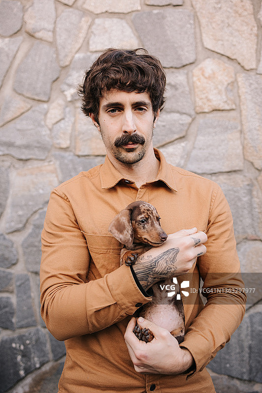 主人怀抱中的迷你巧克力斑点腊肠犬幼犬，手上有纹身图片素材