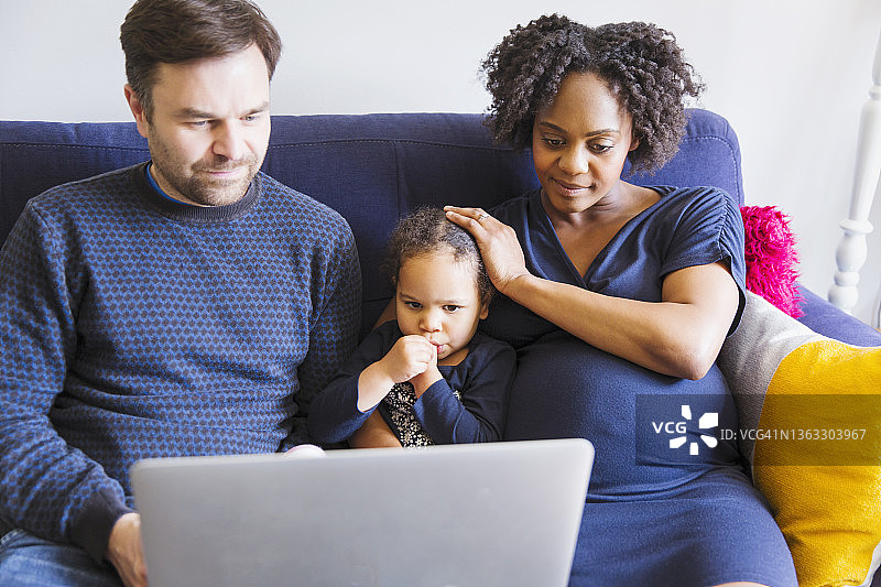 怀孕的家庭在沙发上使用笔记本电脑图片素材