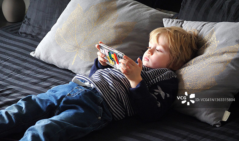 小男孩在床上使用智能手机图片素材