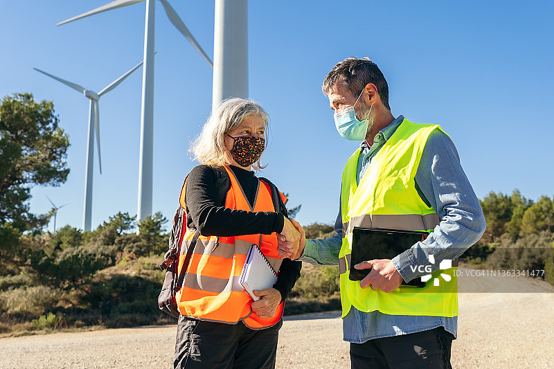 工程师与业主在风力发电场检查风车和风力涡轮机协议（疫情期间）图片素材