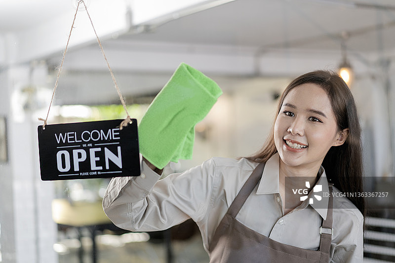 年轻女子在咖啡馆橱窗上悬挂“营业中”标志图片素材