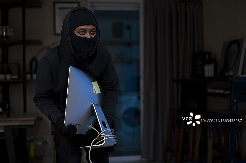 小偷夜间在家中盗窃笔记本电脑图片素材