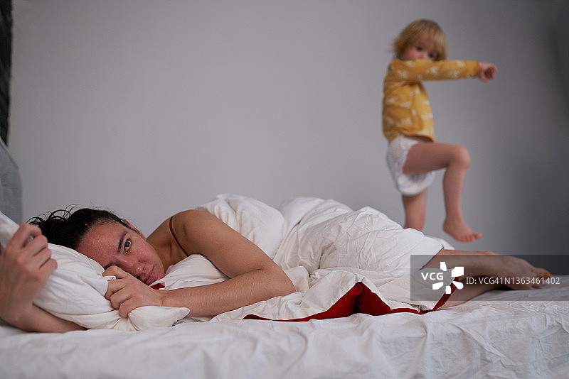 儿童打扰躺在床上的母亲图片素材