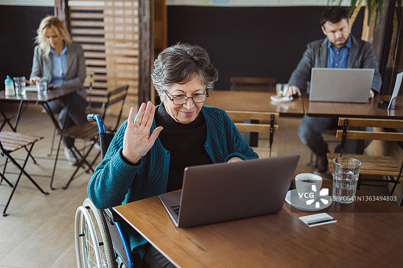 在咖啡馆使用笔记本电脑的快乐残疾妇女图片素材