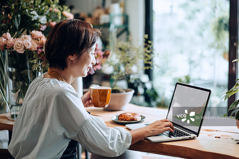 笑容满面的自信亚洲女花店主在笔记本电脑上分析业务图片素材